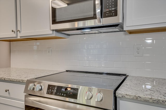interior space with white cabinets, stainless steel appliances, backsplash, and light stone counters