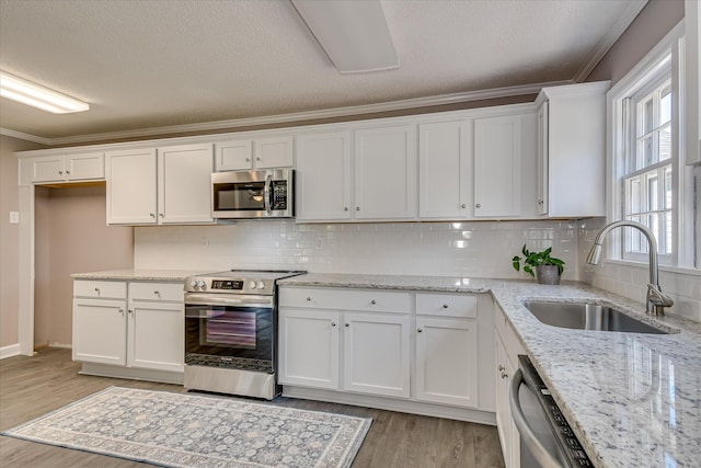 kitchen featuring a sink, light wood-type flooring, stainless steel appliances, white cabinets, and ornamental molding