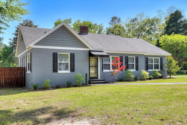 ranch-style house featuring a chimney, fence, a shingled roof, brick siding, and a front yard