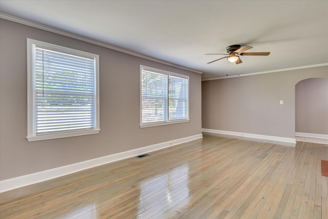 empty room featuring visible vents, ornamental molding, arched walkways, light wood-style flooring, and ceiling fan