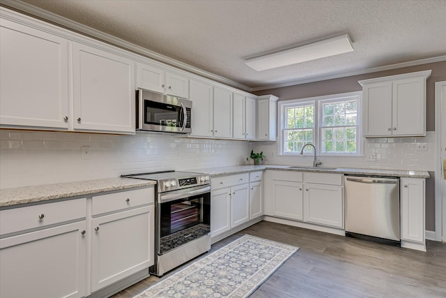 kitchen with stainless steel appliances, a textured ceiling, a sink, backsplash, and white cabinetry