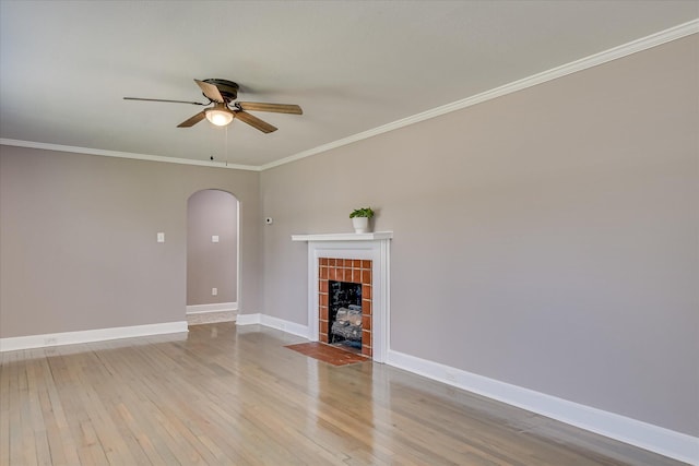 unfurnished living room with a ceiling fan, arched walkways, crown molding, baseboards, and hardwood / wood-style flooring