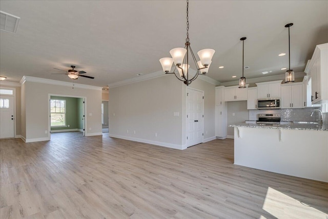 kitchen featuring appliances with stainless steel finishes, ceiling fan with notable chandelier, white cabinetry, ornamental molding, and light stone counters