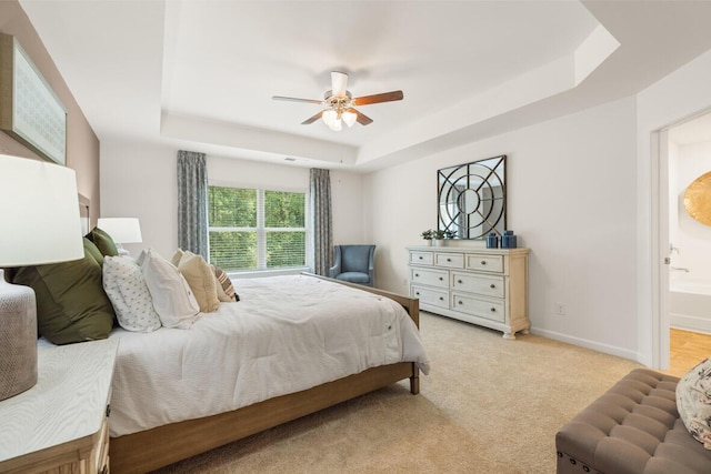 bedroom featuring a tray ceiling, connected bathroom, ceiling fan, and light carpet