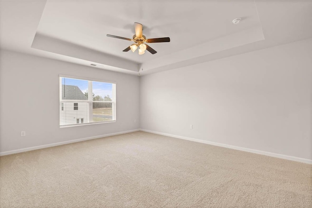 empty room featuring a tray ceiling, ceiling fan, and carpet flooring