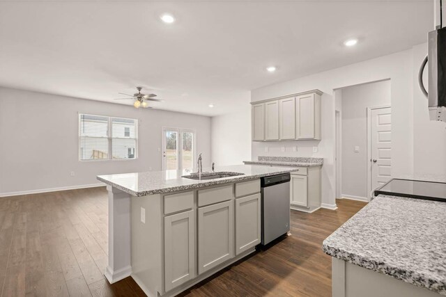 kitchen with light stone countertops, sink, dark wood-type flooring, a center island with sink, and appliances with stainless steel finishes