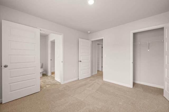 unfurnished bedroom with ensuite bathroom, light carpet, and a closet