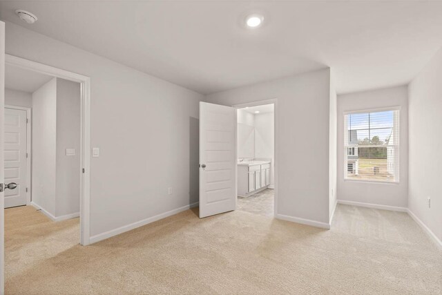 unfurnished bedroom featuring light carpet, ensuite bathroom, and a closet