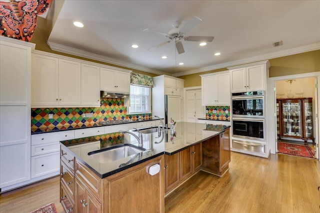 kitchen featuring sink, white cabinets, light hardwood / wood-style floors, stainless steel appliances, and a center island with sink