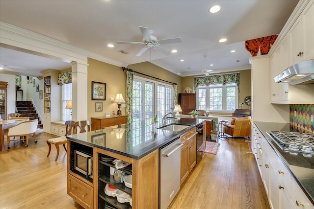 kitchen featuring ceiling fan, appliances with stainless steel finishes, a kitchen island with sink, white cabinets, and ornate columns