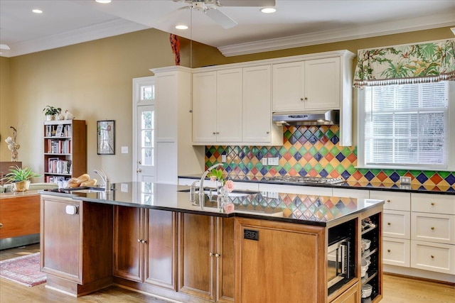 kitchen with stainless steel gas cooktop, sink, ornamental molding, an island with sink, and white cabinets