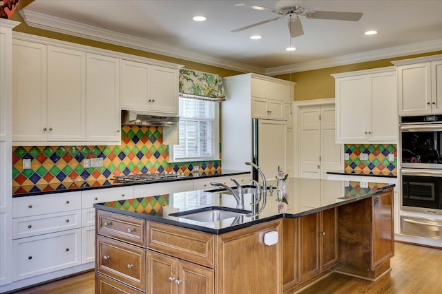 kitchen with sink, ornamental molding, stainless steel appliances, a kitchen island with sink, and white cabinets