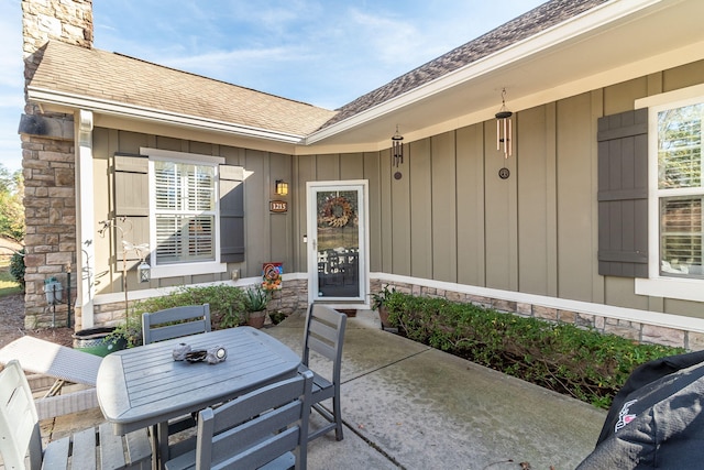 1215 Brookstone Way, Augusta, GA 30909 - view of exterior entry featuring a patio area, outdoor dining area, a shingled roof, stone siding, and a chimney