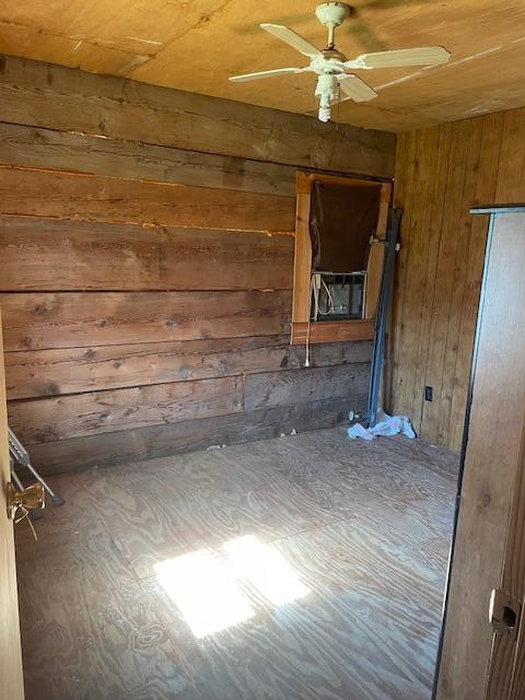 empty room with ceiling fan and wood walls