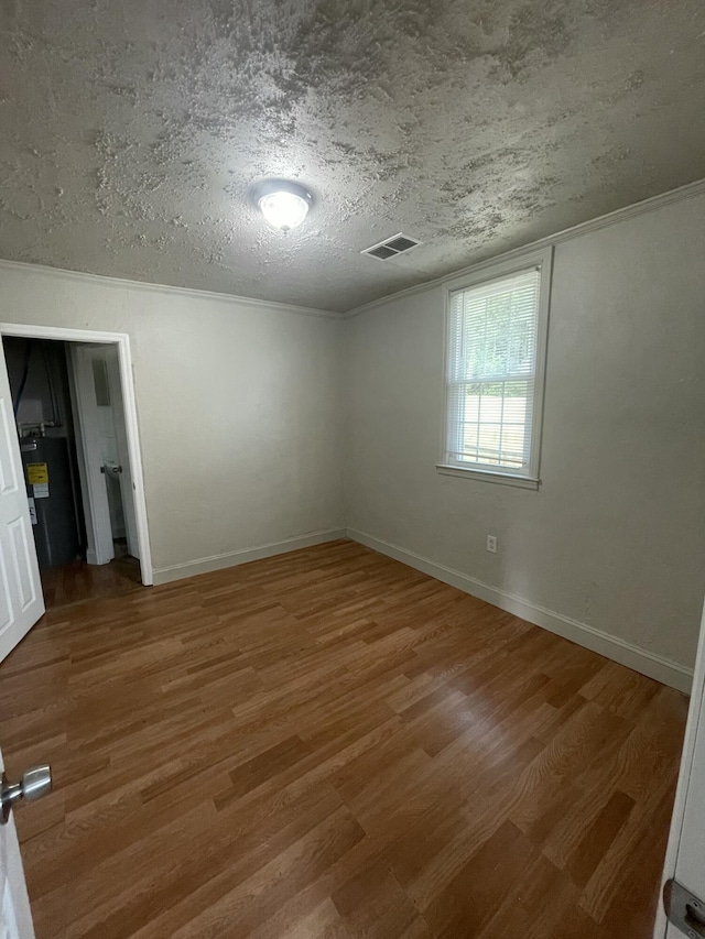 empty room with electric water heater, hardwood / wood-style floors, and a textured ceiling