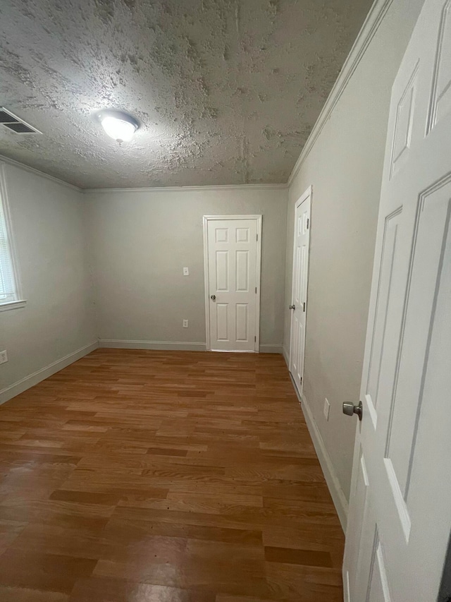 empty room featuring hardwood / wood-style floors, a textured ceiling, and ornamental molding