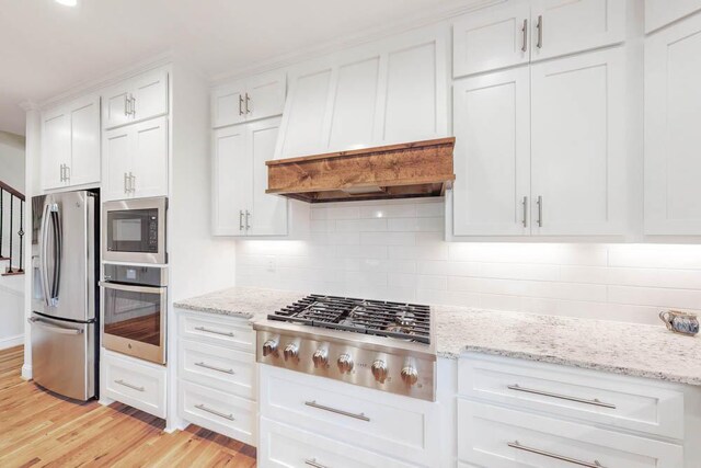 kitchen featuring light stone countertops, backsplash, stainless steel appliances, white cabinets, and light hardwood / wood-style floors