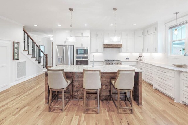 kitchen featuring white cabinets, an island with sink, hanging light fixtures, and appliances with stainless steel finishes