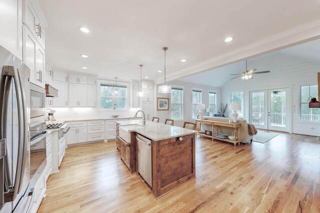 kitchen featuring appliances with stainless steel finishes, light stone counters, a kitchen island with sink, white cabinetry, and hanging light fixtures