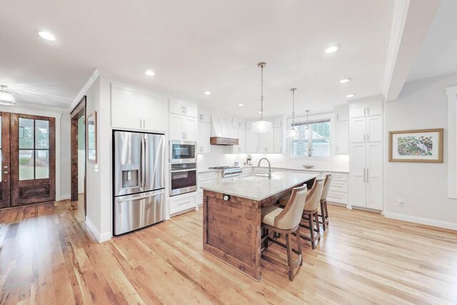 kitchen with light stone countertops, appliances with stainless steel finishes, white cabinetry, and a kitchen island with sink