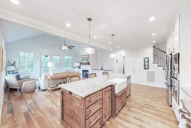 kitchen with light stone counters, a kitchen island with sink, sink, pendant lighting, and white cabinetry