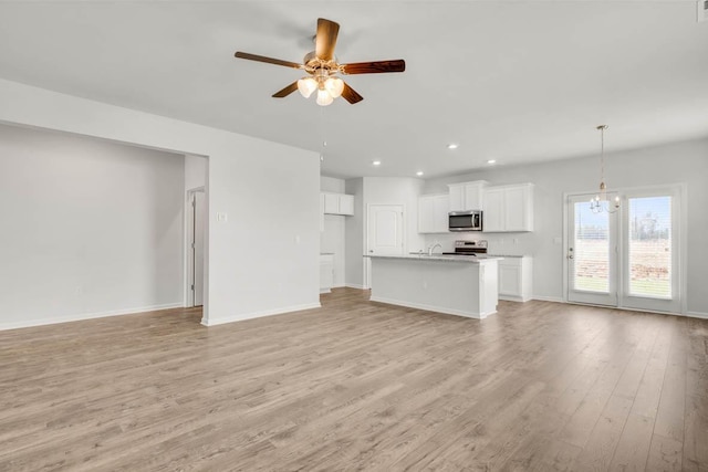 unfurnished living room featuring ceiling fan with notable chandelier and light hardwood / wood-style floors