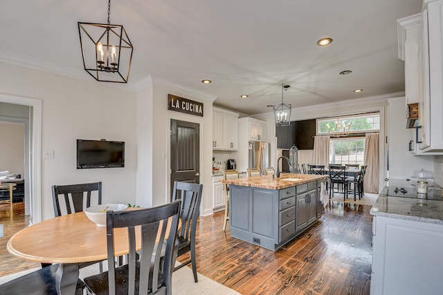 kitchen featuring white cabinets, a center island with sink, light stone countertops, and stainless steel refrigerator