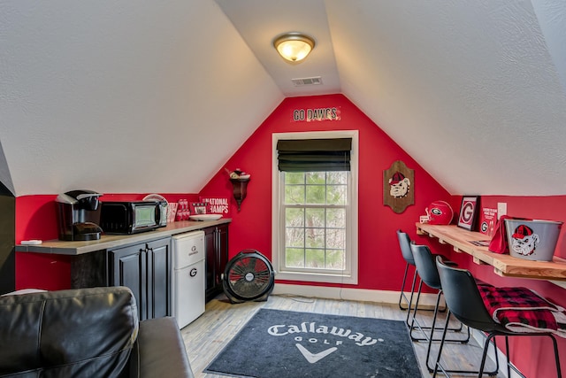 interior space with a textured ceiling, light hardwood / wood-style floors, and vaulted ceiling