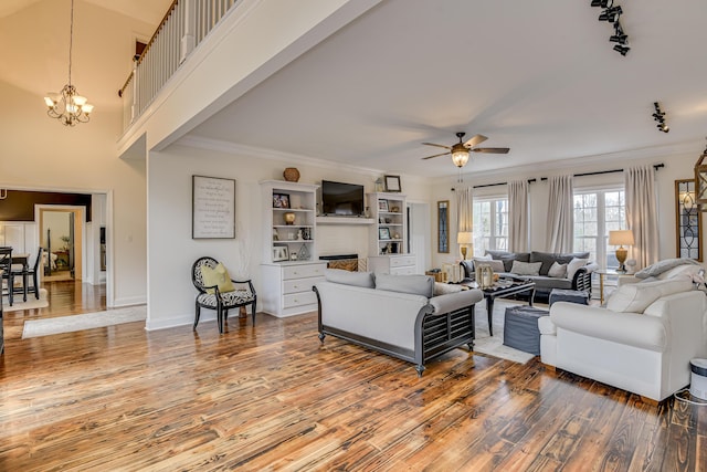 living room with track lighting, ceiling fan with notable chandelier, crown molding, a fireplace, and hardwood / wood-style floors