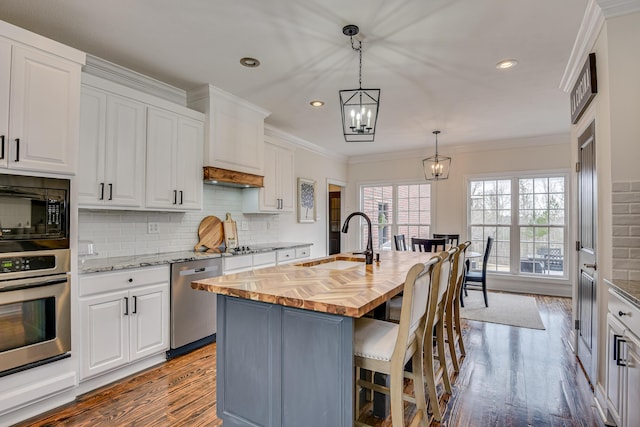 kitchen featuring a center island with sink, white cabinets, butcher block counters, and stainless steel appliances