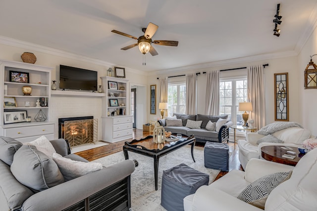 living room featuring rail lighting, ornamental molding, ceiling fan, light hardwood / wood-style flooring, and a fireplace