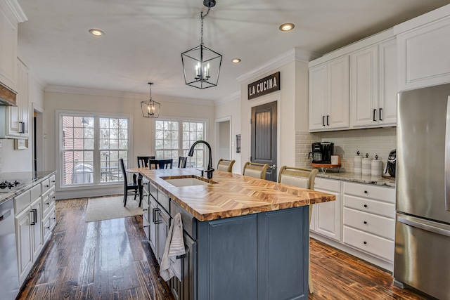 kitchen with wooden counters, pendant lighting, white cabinetry, stainless steel refrigerator, and an island with sink