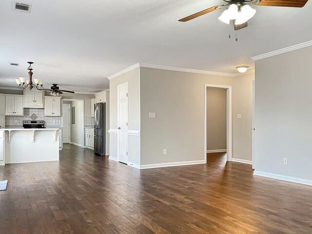 unfurnished living room featuring ceiling fan with notable chandelier, ornamental molding, dark wood-style flooring, and visible vents