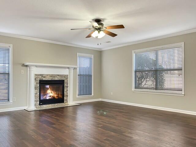 unfurnished living room featuring plenty of natural light, a premium fireplace, crown molding, and dark wood-type flooring