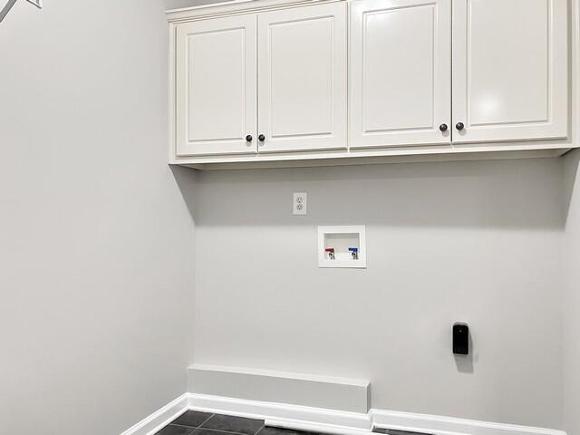 clothes washing area with hookup for a washing machine, dark tile patterned flooring, cabinet space, and baseboards