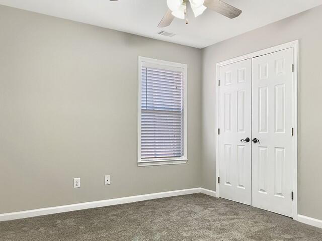 unfurnished bedroom with baseboards, visible vents, a ceiling fan, dark colored carpet, and a closet