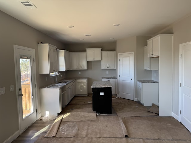 kitchen featuring a kitchen island, light stone countertops, white cabinetry, and sink