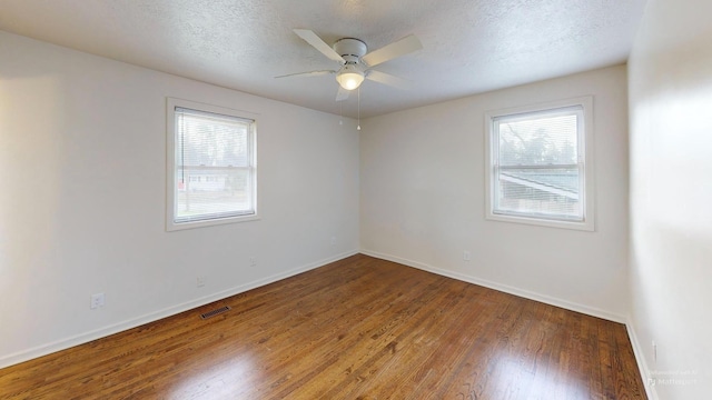 empty room with a textured ceiling, visible vents, a wealth of natural light, and wood finished floors