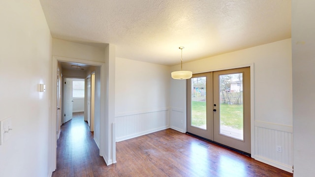 unfurnished dining area featuring french doors, wainscoting, visible vents, and dark wood-style flooring