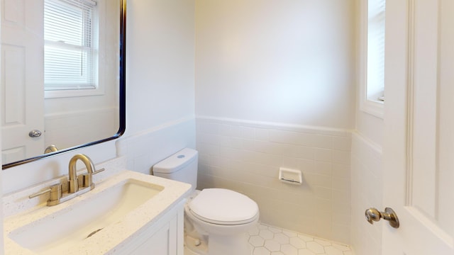 bathroom with toilet, a wainscoted wall, tile walls, and vanity