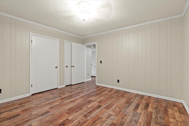 249 Usher Rd, Waynesboro, GA 30830 - unfurnished bedroom with wood finished floors, multiple closets, ornamental molding, a textured ceiling, and wood walls