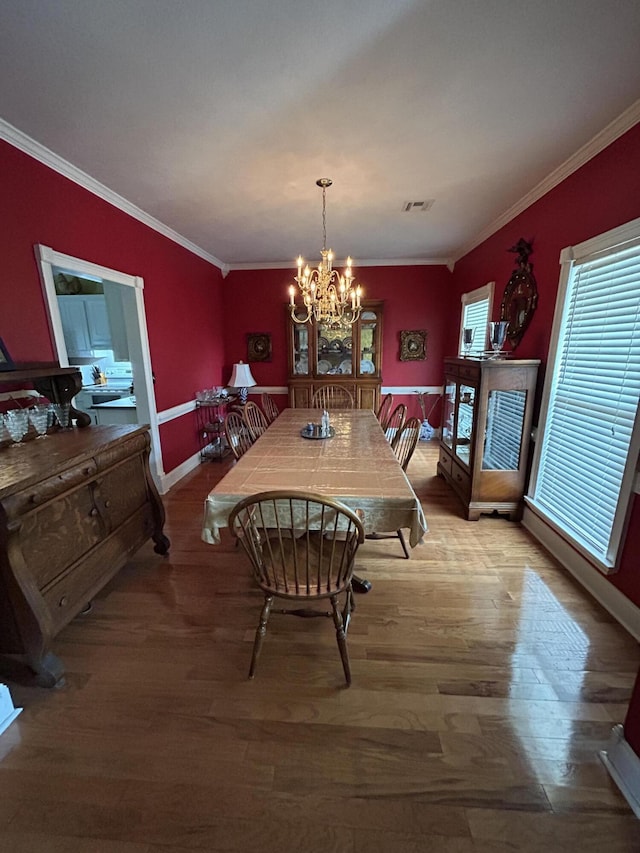 dining area with a chandelier, baseboards, ornamental molding, and wood finished floors