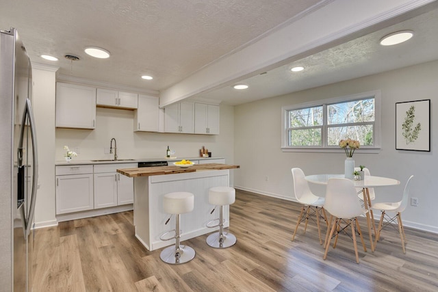 kitchen featuring wood counters, stainless steel fridge, sink, white cabinets, and light hardwood / wood-style floors