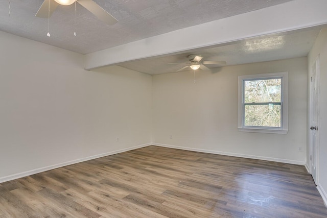 empty room with beamed ceiling, a textured ceiling, and hardwood / wood-style flooring