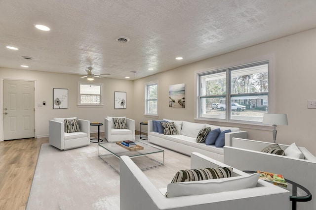 living room with a textured ceiling, light hardwood / wood-style flooring, and ceiling fan