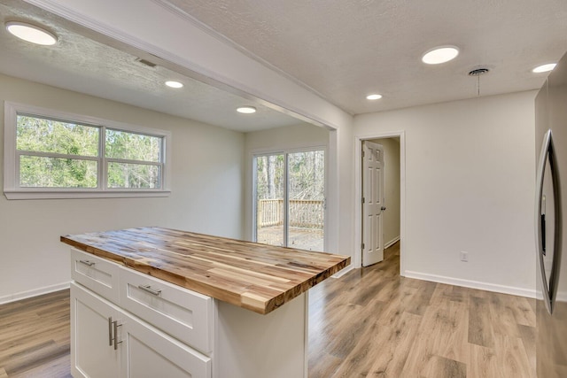 kitchen with white cabinetry, light hardwood / wood-style flooring, wooden counters, a textured ceiling, and a kitchen island