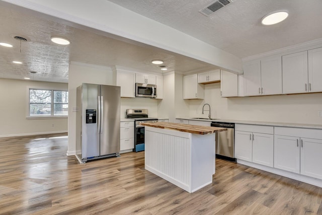 kitchen featuring sink, white cabinetry, appliances with stainless steel finishes, light hardwood / wood-style floors, and butcher block counters