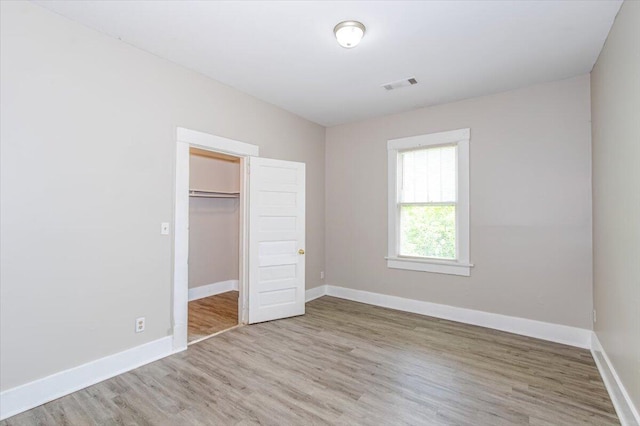 unfurnished bedroom with hardwood / wood-style floors, a walk in closet, and a closet