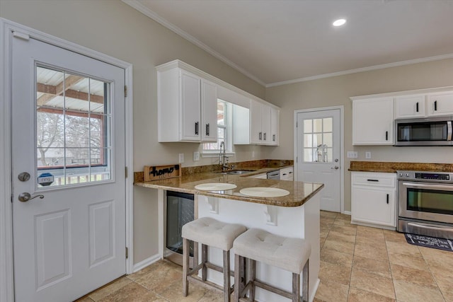 kitchen with stainless steel appliances, ornamental molding, white cabinetry, a sink, and beverage cooler