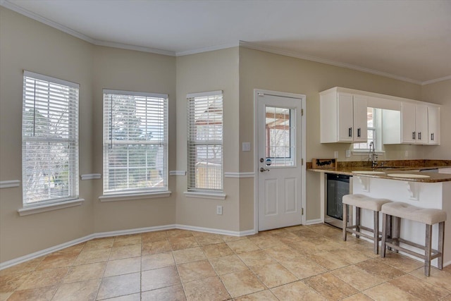 kitchen with baseboards, ornamental molding, white cabinets, beverage cooler, and a kitchen breakfast bar